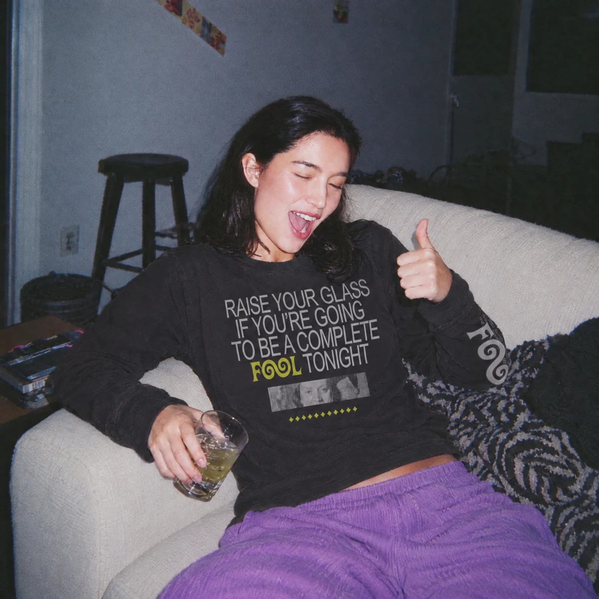 A friend laughing on the sofa in a Fool's Fix jumper, giving a thumbs up