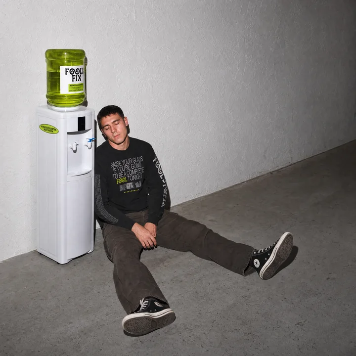 A man sitting on the floor beside the Fool's Fix water cooler