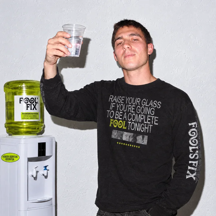 A man raising a cup of water next to the Fool's Fix water cooler